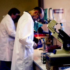 Photograph of lab microscope with two lab technicians in the background