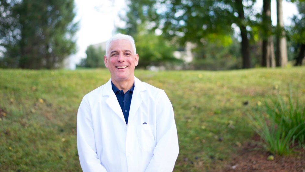 A man in a lab coat smiling in a grassy field at Wholesale Optical Frames.