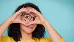 A woman with glasses forming a heart shape with her hands. Wholesale Optical Lab USA.