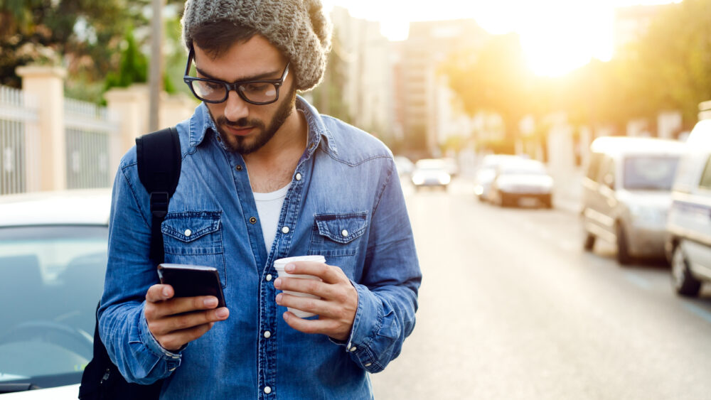 A man in a hat and glasses holding a cell phone. Wholesale Optical Lab USA.