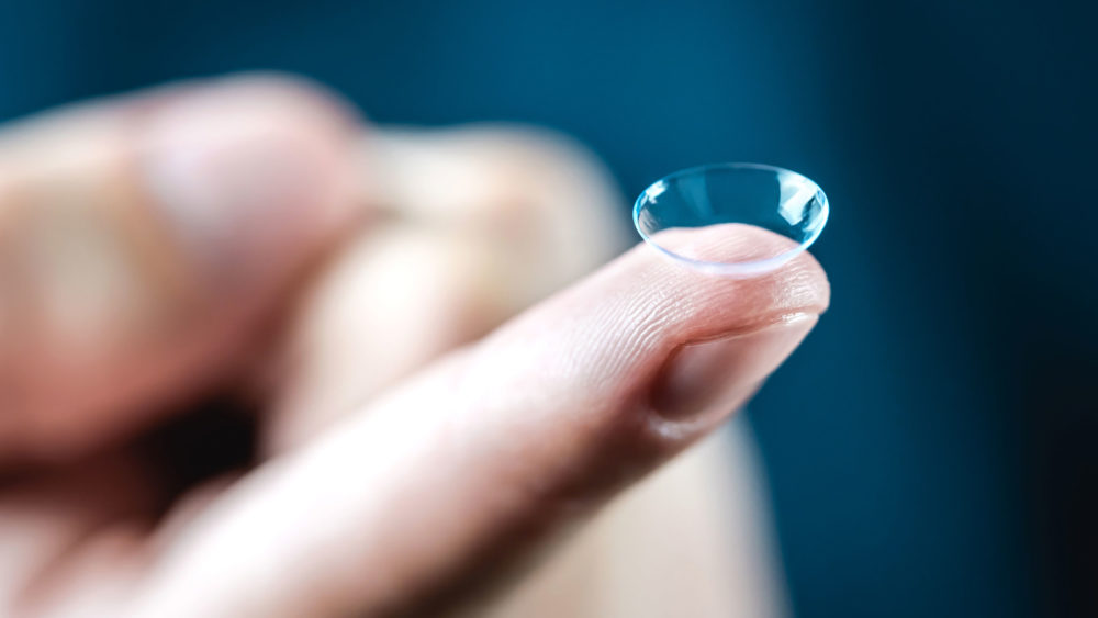 A person holding a tiny contact lens, perfect for clear vision. Get quality optical lenses from manufacturers in the USA