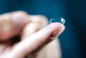 A person holding a tiny contact lens, perfect for clear vision. Get quality optical lenses from manufacturers in the USA