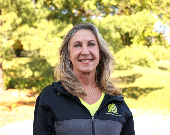 Lori Fioravanti, an Optical Frames Allentown representative, standing confidently in front of trees wearing a striking black and yellow jacket.