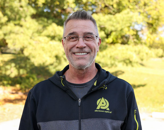 Meet Tim Goodin, the delivery expert from Deliveries & Shipping Optical Lenses, sporting a black jacket and green hoodie with a cheerful grin.