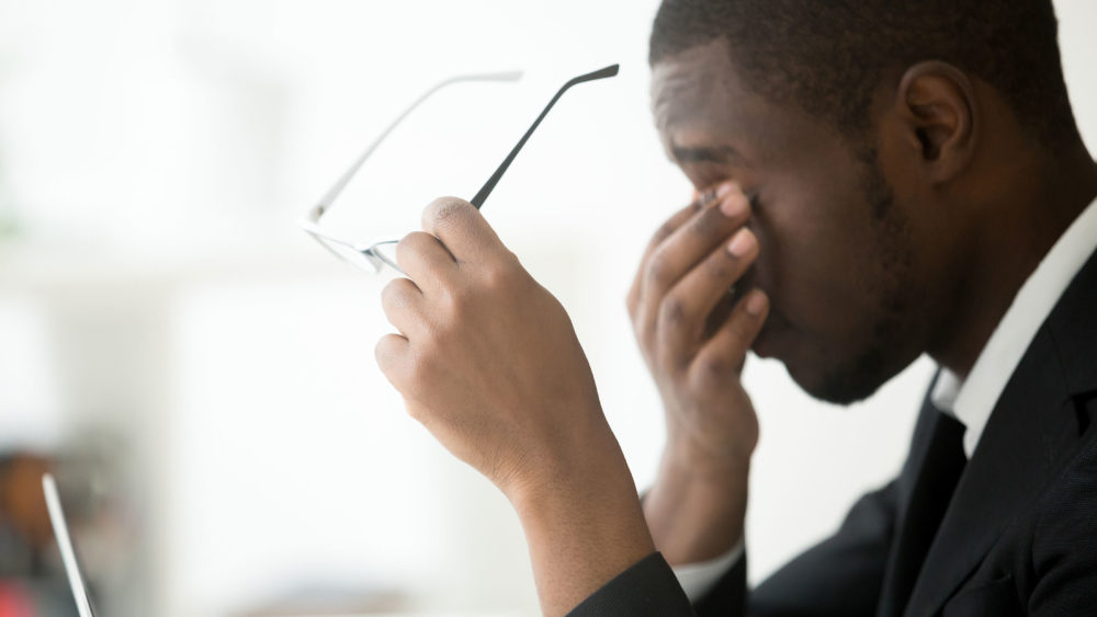 A man feels the affects of stress as he holds his glasses to rub his strained eyes.