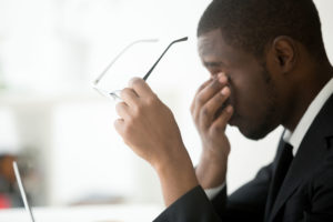 A stressed man in a suit holding his head, feeling overwhelmed by the pressure. Stress Affects Vision Optical Lenses.