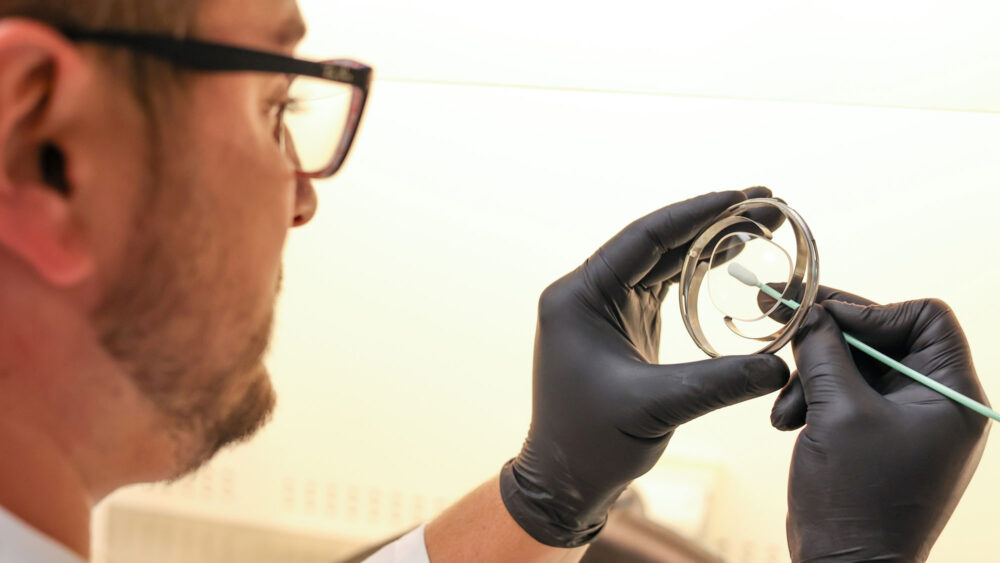 At Wholesale Optical Labs, a man in a lab coat holds a small object.